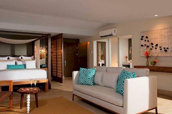 Schlafzimmer im Secrets Papagayo Costa Rica mit einem Bett, Kissen und einem Wohnzimmerbereich.