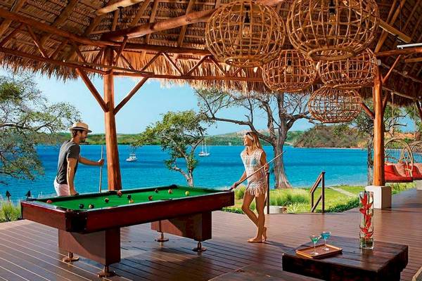 Mann und Frau spielen Pool auf Holzdeck mit Meerblick im Secrets Papagayo Costa Rica