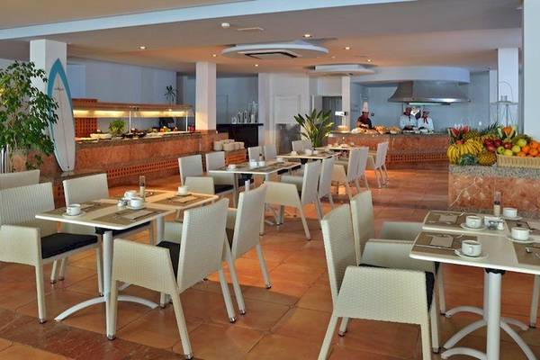 Restaurant des Sol Wave House All Suites mit vielen Tischen und Stühlen, serviertem Frühstück und Köchen im Hintergrund.