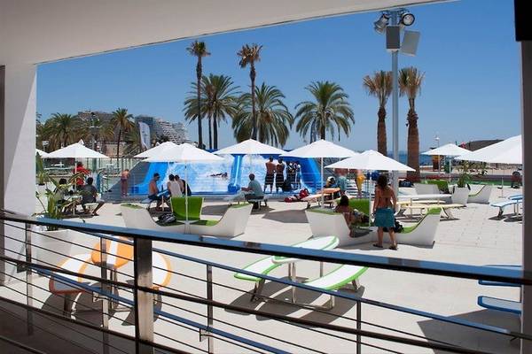Ausblick auf einen Strand mit Umkleidekabinen und Umbrellas, wo Gäste sitzen und eine Wasserrutsche im Hintergrund ist.