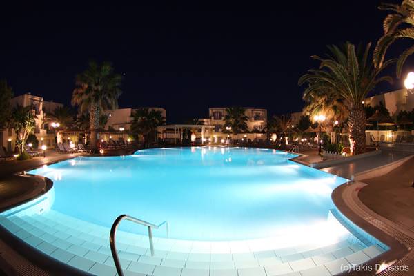 Nachtansicht des Europa Beach Hotel & Spa mit beleuchtetem Pool und umgebenden Palmen.