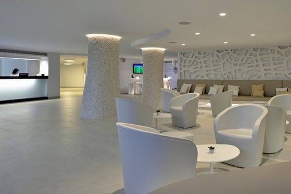 Hotellobby des Sol Wave House All Suites mit weißen Möbeln und einer großen Couch.
