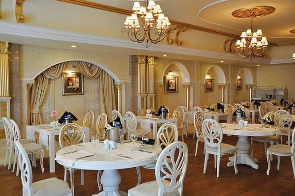 Das elegante Restaurant des Nirvana Dolce Vita Hotels mit weißen Tischen und Stühlen, Kronleuchtern und dekorativen Wandbildern.