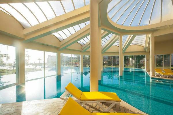 Innenpool des Mahdia Beach & Aqua Park Hotels mit gelben Liegestühlen und Glasdach.