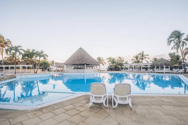 Außenpool des Iberostar Origin Bella Costa Hotels mit weißen Liegestühlen und Palmen.