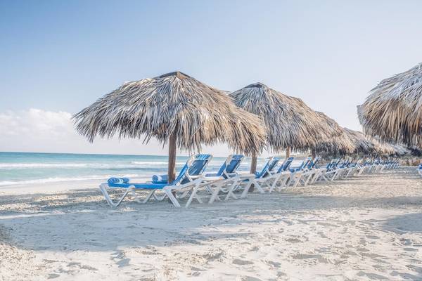 Reihe von Liegen unter Strohschirmen am Strand des Iberostar Origin Bella Costa Hotels