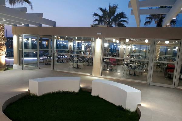 Außenterrasse des Europa Beach Hotel & Spa mit Gästen an Tischen und Palmen im Hintergrund.