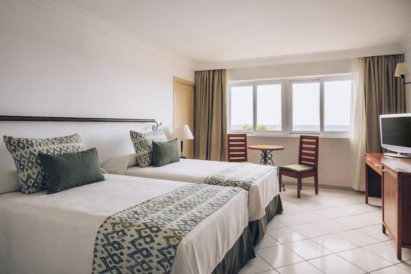 Doppelzimmer im Iberostar Origin Bella Costa mit zwei Betten, Dekor und Meerblickfenstern.