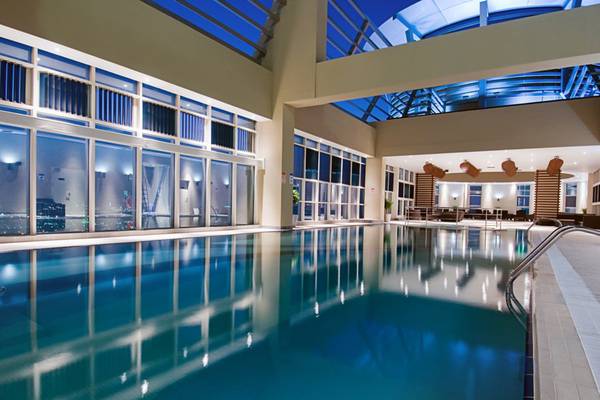 Innenpool des Grand Millennium Al Wahda Hotels bei Nacht mit Stadtblick