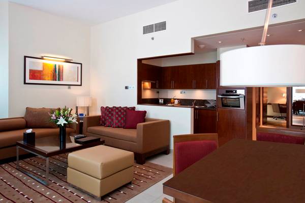 Wohnzimmer im Grand Millennium Al Wahda Hotel mit Sofas, Tisch, Lampe und Gemälde.