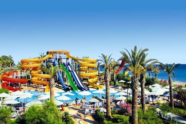 Wasserpark des Long Beach Alanya Hotels mit mehreren Rutschen und vielen Sonnenschirmen.
