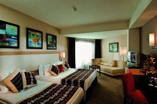 Doppelzimmer im Long Beach Alanya Hotel mit zwei Betten, Couch, Fernseher und Gemälden an der Wand.