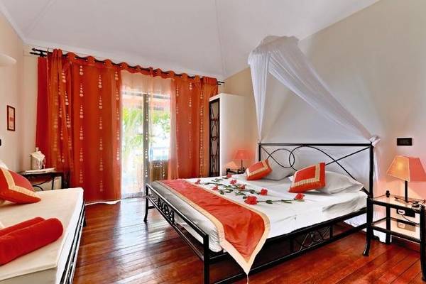 Ein Schlafzimmer im Nakai Maayafushi Resort mit einem Doppelbett und einem Sofa, beide mit roten Kissen und weißen Laken.
