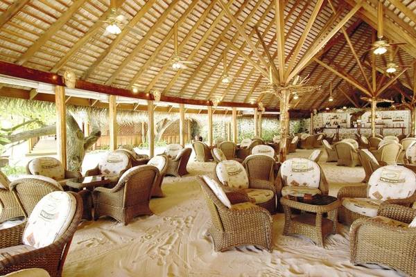 Innenbereich des Nakai Maayafushi Resorts mit vielen Rattan-Stuhlreihen und Tischen auf einem Sandboden.