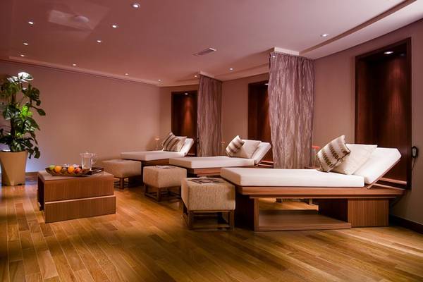 Spa-Lounge im Grand Millennium Al Wahda Hotel mit weißen Liegen und Holzmöbeln.