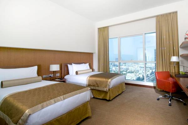 Zwei Betten in einem Hotelzimmer des Grand Millennium Al Wahda mit Stadtblick