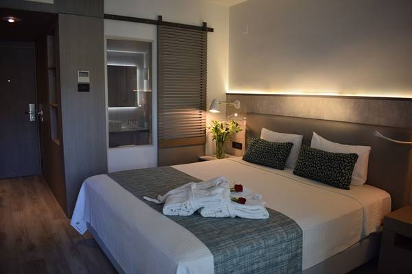 Ein geräumiges Zimmer im Minos Mare Hotel mit einem Bett, Kissen und Handtüchern, die elegant auf dem Bett liegen.