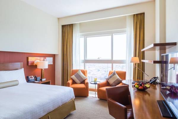 Hotelzimmer im Grand Millennium Al Wahda mit Doppelbett, zwei Sesseln, Schreibtisch und Aussicht.