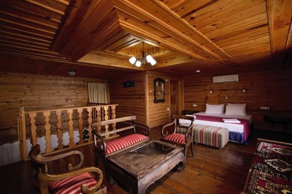 Innenansicht eines Holzzimmers im Marble Arch Hotel in Datca mit Bett, Sofa, Tisch und Holzbalken.