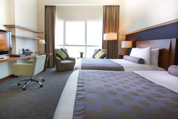 Doppelbett-Zimmer im Grand Millennium Al Wahda mit Fernseher, Schreibtisch und zwei Sesseln.