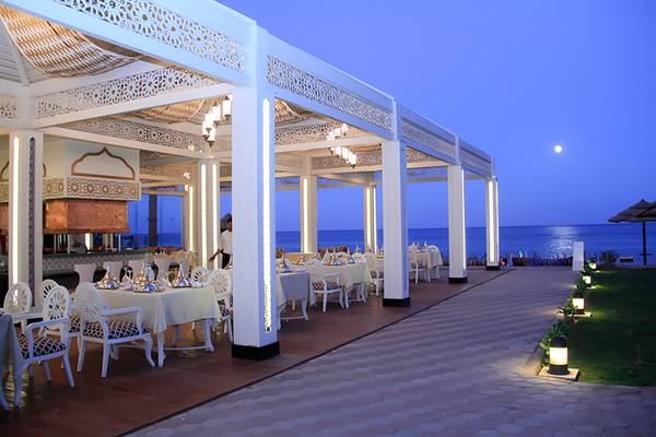Draußen sitzende Gäste an Tischen im Freien des Rixos Sharm El Sheikh Hotels mit Blick auf das Meer bei Nacht.