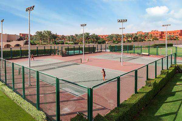 Tennisplatz im Rixos Sharm El Sheikh Hotel mit Spielern und Gebäuden im Hintergrund.