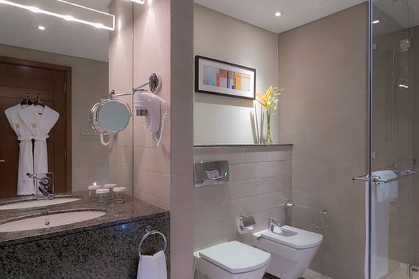 Badezimmer im Grand Millennium Al Wahda Hotel mit Waschbecken, Spiegel, Toilette und Dusche