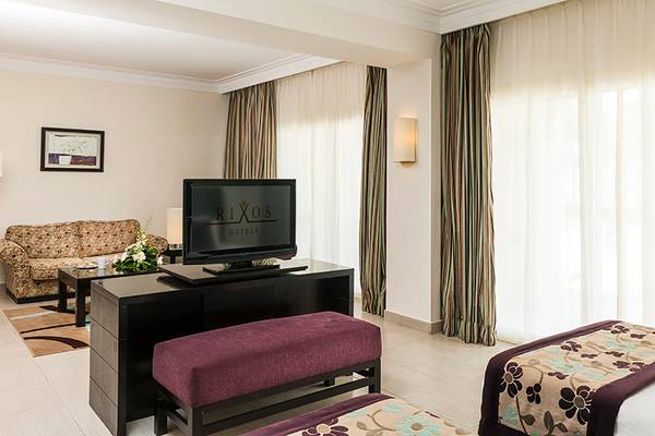 Ein modernes Hotelzimmer im Rixos Sharm El Sheikh mit Fernseher, Sofa, Tisch und zwei Betten.