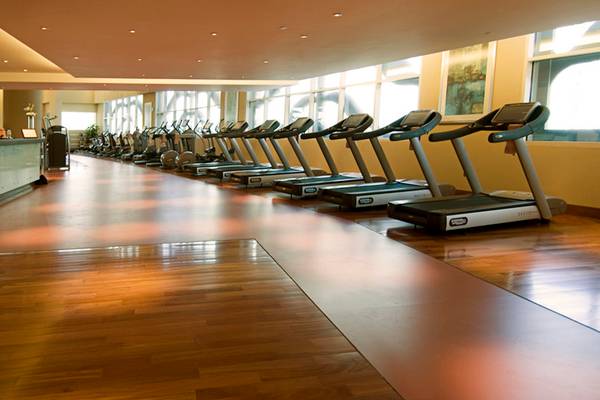 Fitnessstudio im Grand Millennium Al Wahda Hotel mit mehreren Laufbändern und hellen Holzböden.