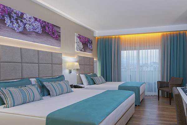 Zwei Betten in einem Hotelzimmer des Asia Beach Resort & Spa mit Früchten und Blumen auf dem Schreibtisch.