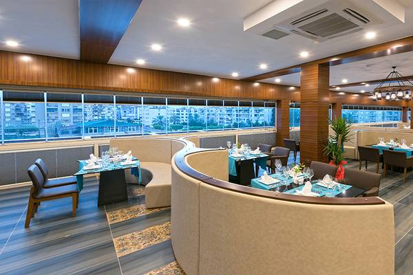Innenansicht des Restaurants im Asia Beach Resort & Spa mit runden Tischen und Stühlen, umgeben von großen Fenstern.