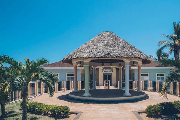 Außenansicht des Iberostar Laguna Azul Hotels mit strohdeckigem Pavillon und bunten Zäunen.
