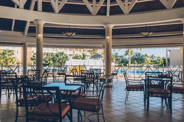 Innenbereich des Iberostar Laguna Azul Hotels mit vielen Tischen und Stühlen, gesäumt von Säulen und einer Glasfassade.