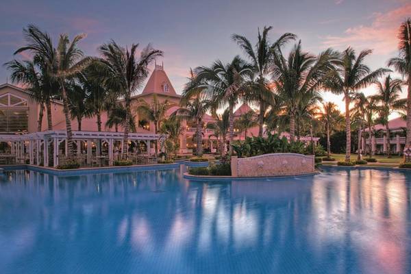 Ein großer Swimmingpool im Sugar Beach Mauritius Hotel, umgeben von Palmen und Gebäuden.