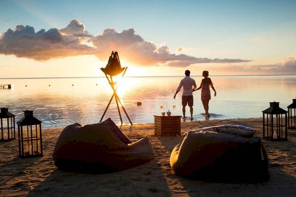 Paar am Strand von Sugar Beach Mauritius während des Sonnenuntergangs mit Laternen und Wasser im Hintergrund.