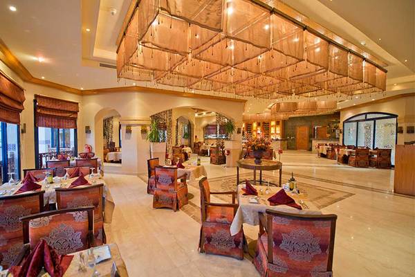 Innenansicht des Restaurants des Amphoras Beach Hotels mit gemusterten Stühlen, Tischdecken und einer großen Deckenleuchte.