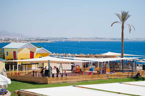 Spielplatz am Strand des Amphoras Beach Hotels mit gelben Hütten und Palmen im Hintergrund.