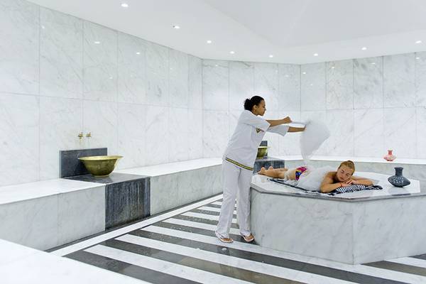 Eine Frau im weißen Outfit serviert einem Gast im Whirlpool im Spa-Bereich des Amphoras Beach Hotels.