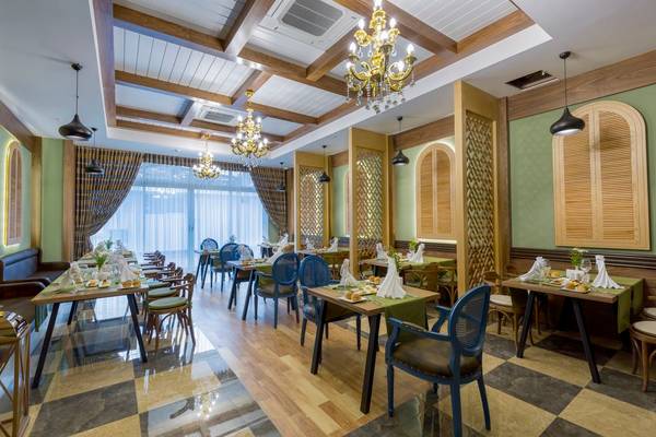 Innenbereich eines Restaurants im Side Royal Palace Hotel & Spa mit runden Tischen, Stühlen und grünen Tischdecken.