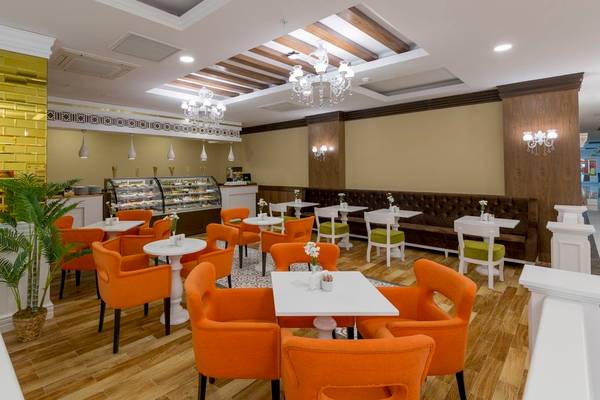 Innenbereich des Cafes im Side Royal Palace Hotel & Spa mit orangefarbenen Stühlen und weißen Tischen.