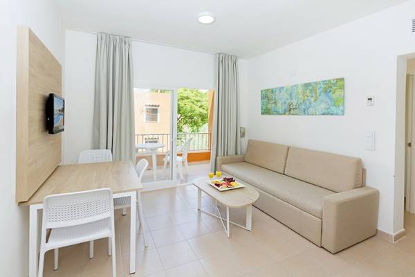 Wohnbereich des HSM Club Torre Blanca Hotels mit Couch, Tisch, Fernseher und Balkonzugang.