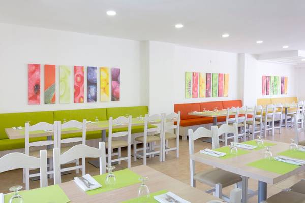 Innenansicht des Restaurants im HSM Club Torre Blanca mit grün und orangefarbenen Möbeln und farbenfrohen Wandbildern.
