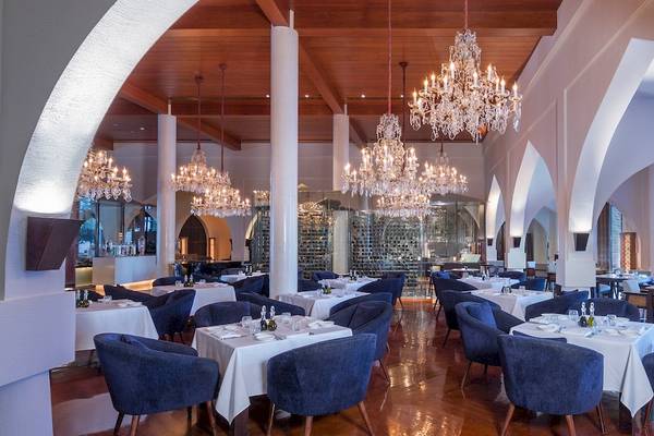 Innenansicht des Restaurants im The Chedi Muscat mit blauen Stühlen, weißen Tischen und Kronleuchtern.