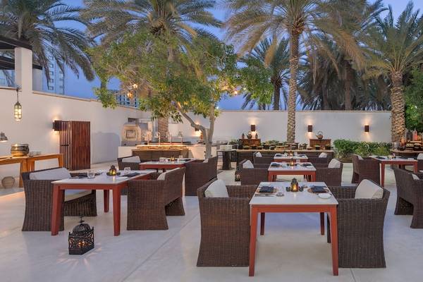 Außenbereich des Chedi Muscat Hotels mit Tischen und Stühlen unter Palmen