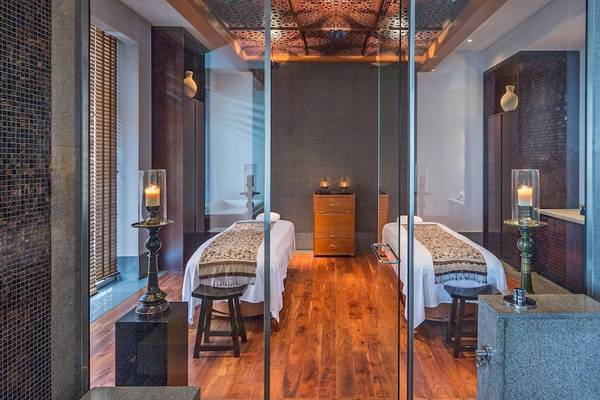 Spa-Behandlungsraum im Chedi Muscat mit zwei Behandlungstischen, Kerzen und Holzboden.