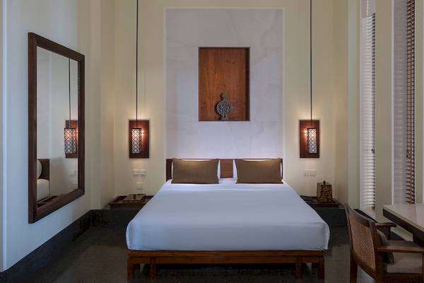 Schlafzimmer im Chedi Muscat mit einem großen Bett, zwei Kissen, einem Schreibtisch, einem Stuhl und einem Spiegel.