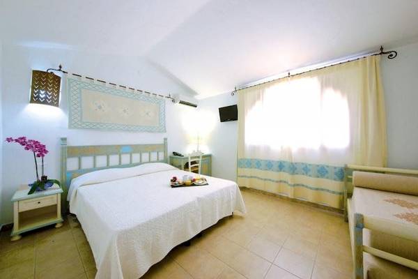 Innenansicht eines Schlafzimmers im Alma Resort mit Bett, Nachttischen und Fernseher.