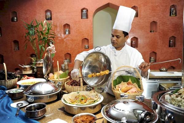 Ein Koch bereitet Speisen auf einem Grill zu, während er in der Küche des Shangri-La Barr Al Jissah Resorts & Spa steht.