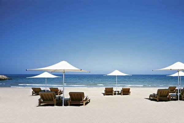 Strand mit Holzstühlen und Schirmen im Shangri-La Barr Al Jissah Resort