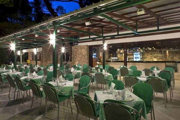 Außenbereich des BlueSun Hotel Berulia mit grünen Tischen und Stühlen unter einer überdachten Terrasse.
